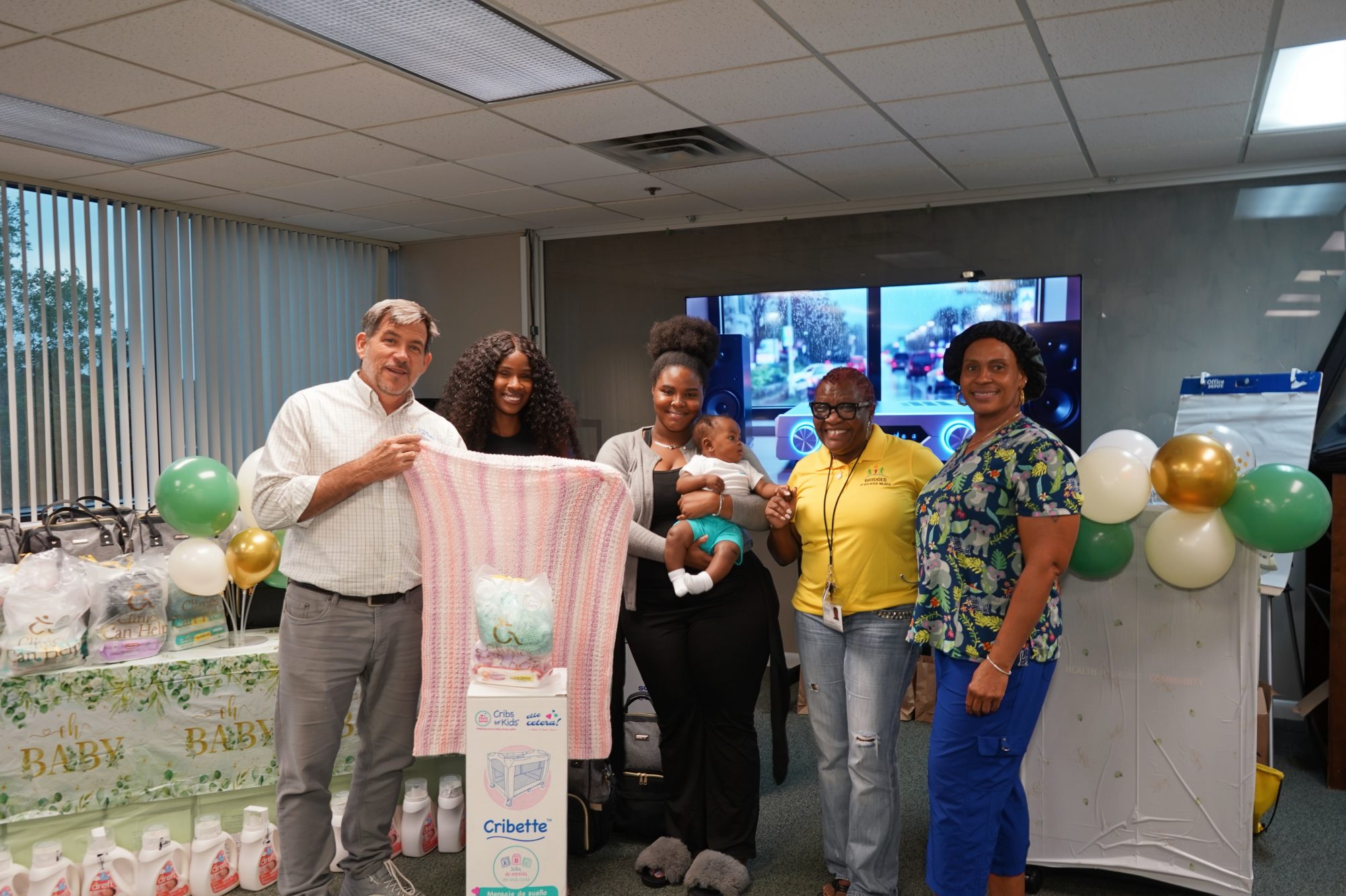 Owen O'Neill, Lottie Moise, Akeelah Jackson holding a baby, and Angela Kelly posing together indoors by a Cribette box and baby supplies.