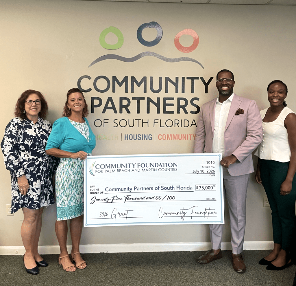 Community Partners of South Florida Receives $75K Grant for Economic Mobility Four professionals standing in front of a Community Partners of South Florida wall logo, holding a large $75,000 ceremonial grant check dated July 10, 2026.