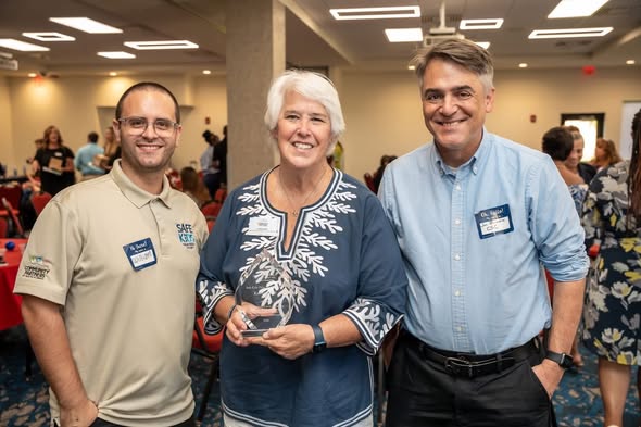 Three smiling individuals, including Kathy holding a crystal award, posing together at the FAU CARD Autism Leaders Brunch in Palm Beach County.