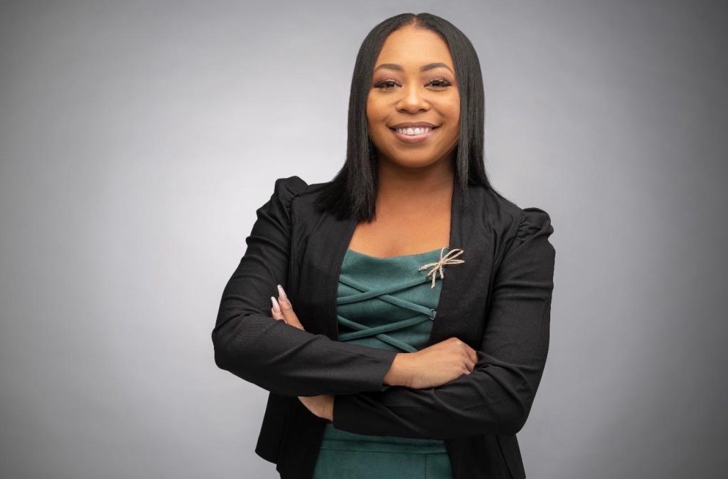 Jade Lawson, newly appointed Board Member for Community Partners of South Florida. Headshot of Jade Lawson smiling with arms crossed, wearing a black blazer over a green dress with a dragonfly brooch.