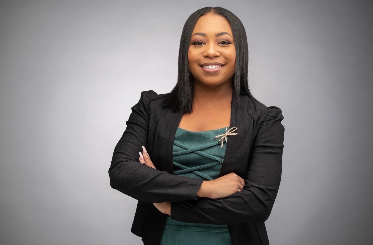 Headshot of Jade Lawson smiling with arms crossed, wearing a black blazer over a green dress with a dragonfly brooch.