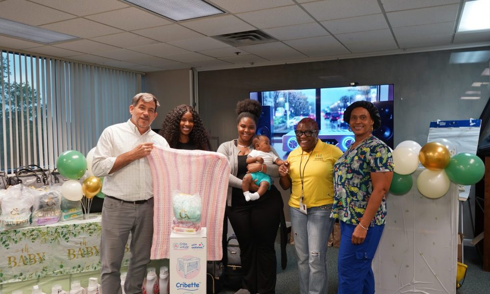Owen O'Neill, Lottie Moise, Akeelah Jackson holding a baby, and Angela Kelly posing together indoors by a Cribette box and baby supplies.