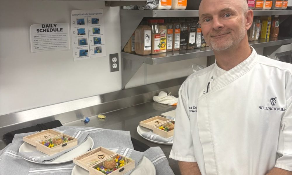 Chef Joshua Crane of Wellington Bay standing proudly in a commercial kitchen next to plated portions of his gourmet Pani Puri entry.