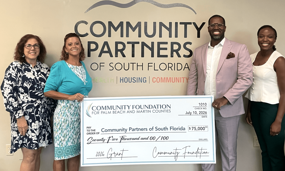 Four professionals standing in front of a Community Partners of South Florida wall logo, holding a large $75,000 ceremonial grant check dated July 10, 2026.